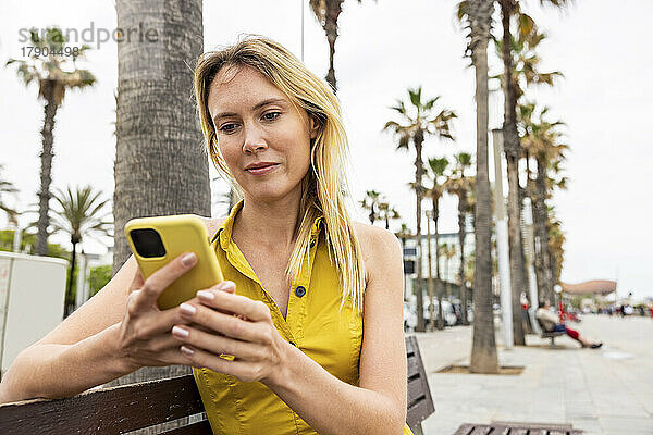 Frau sitzt auf Bank und benutzt Smartphone