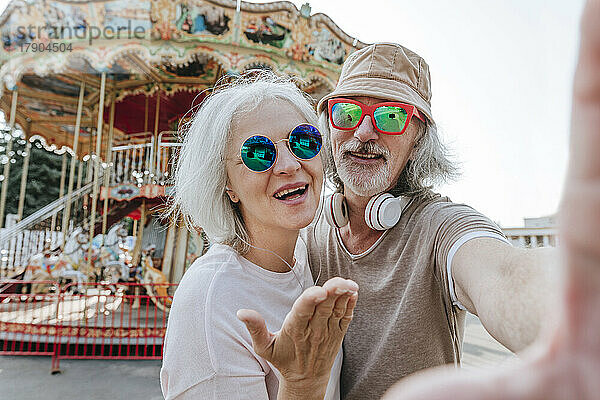 Älterer Mann und reife Frau machen Selfie vor Karussell im Vergnügungspark