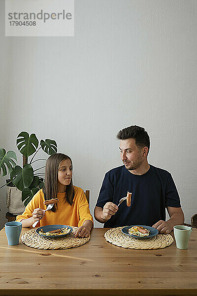 Lächelndes Mädchen mit Vater beim Frühstück am Esstisch