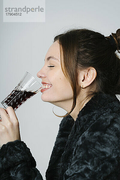 Lächelnde Frau trinkt Rotwein im Studio