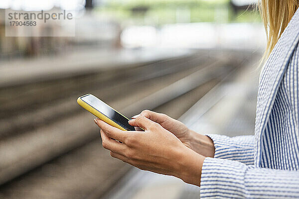 Hände einer Geschäftsfrau  die ihr Smartphone am Bahnhof benutzt