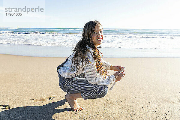 Glückliches Mädchen in hockender Position am Strand