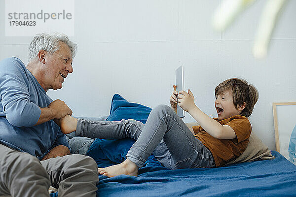Glücklicher Junge fotografiert Großvater mit Tablet-PC auf dem heimischen Sofa