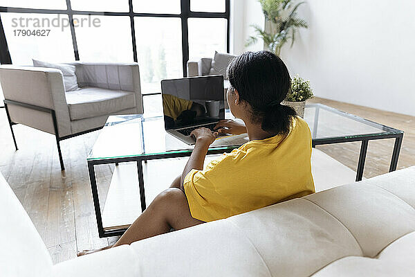 Frau sitzt im Wohnzimmer und arbeitet von zu Hause aus mit Laptop