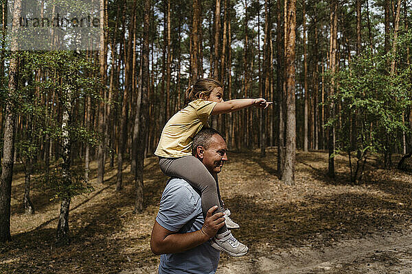 Reifer Mann trägt Mädchen auf Schultern und geht im Wald spazieren