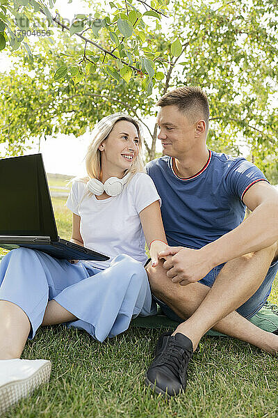 Junge Frau sitzt mit Laptop und hält die Hand ihres Freundes im Park