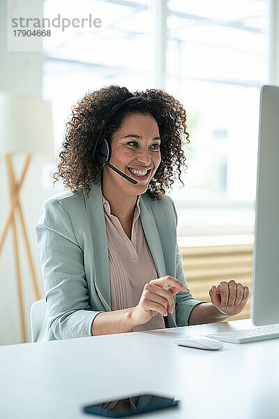 Happy customer service representative discussing through headset at workplace