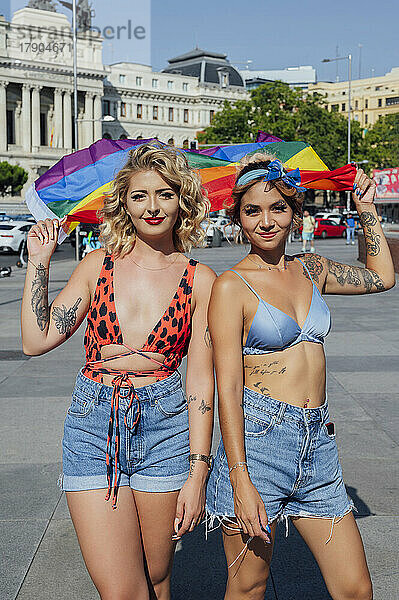 Freunde stehen mit Regenbogenfahne auf Fußweg