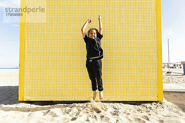 Fröhlicher Junge springt vor einer gelben Wand am Strand