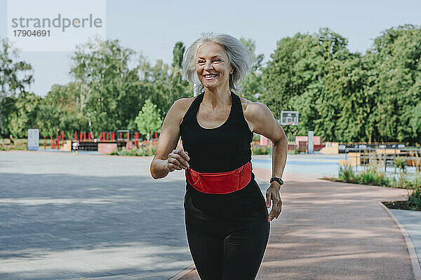 Glückliche reife Frau mit Hosenbund joggt im Park