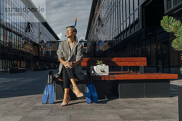 Glückliche Geschäftsfrau mit Schnorchel sitzt auf einer Bank im Büropark