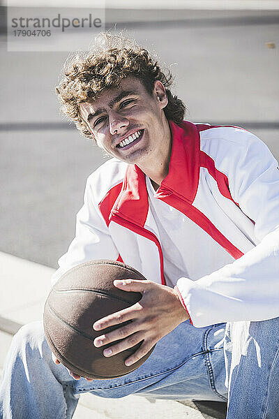 Happy young man holding basketball on sunny day