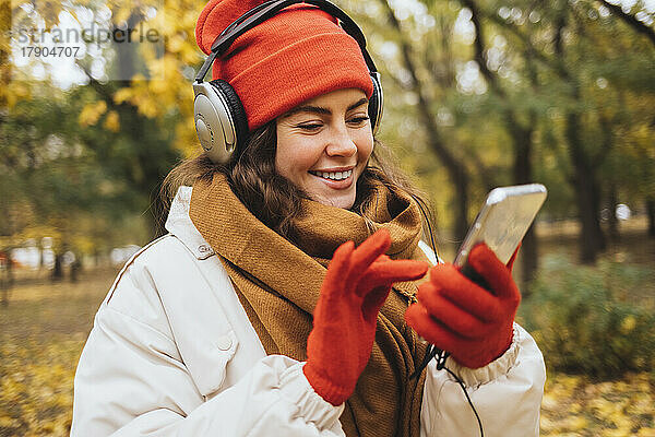 Lächelnde Frau  die im Park Musik über Kopfhörer mit Smartphone hört