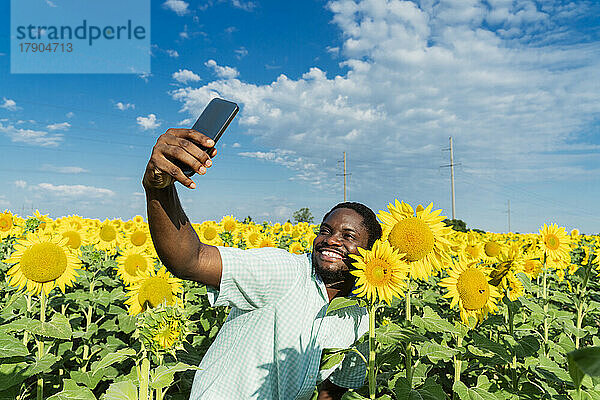Glücklicher Mann mit Sonnenblume  der im Feld ein Selfie mit dem Handy macht