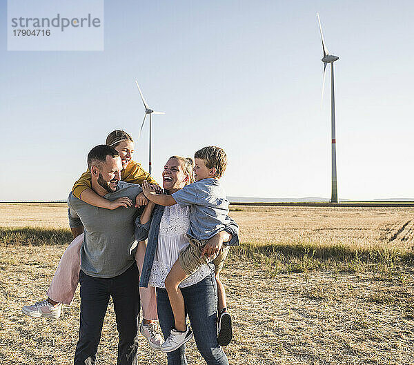 Selbstbewusste Familie steht im Windpark und trägt Kinder