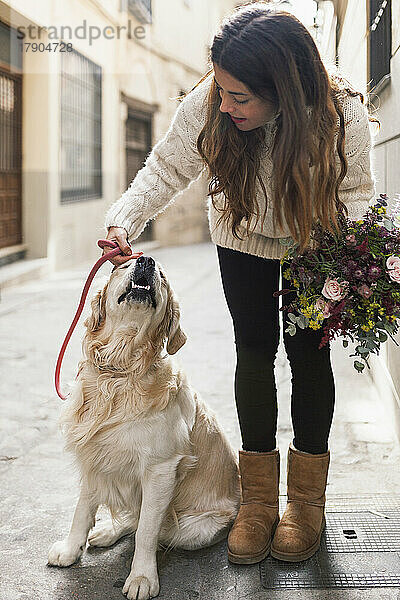 Frau hält Blumenstrauß in der Hand und streichelt Hund in Gasse