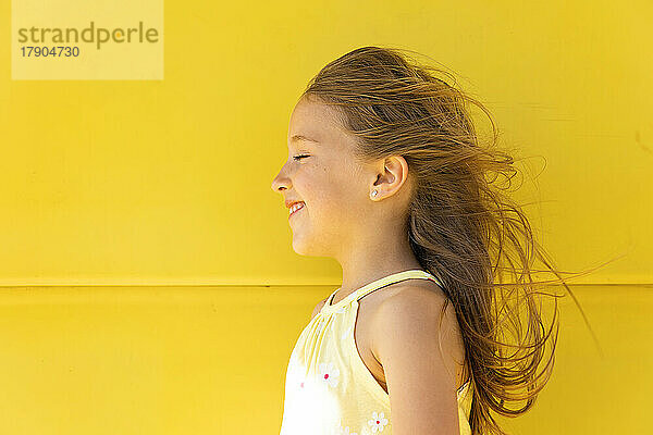 Happy girl with long hair standing in front of yellow wall