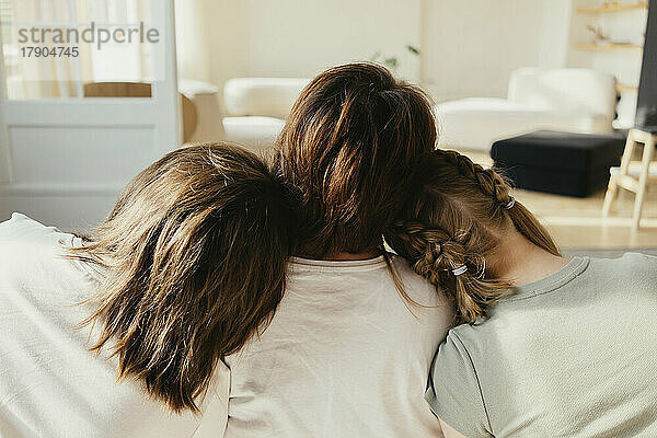 Geschwister lehnen ihre Köpfe an die Schulter der Mutter im heimischen Wohnzimmer