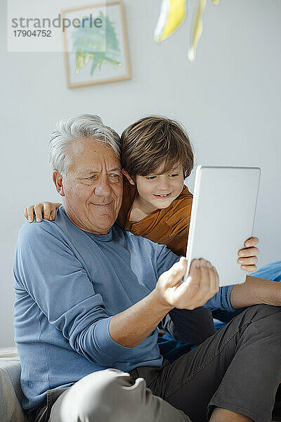 Lächelnder Junge  der zu Hause ein Selfie mit seinem Großvater über einen Tablet-Computer macht