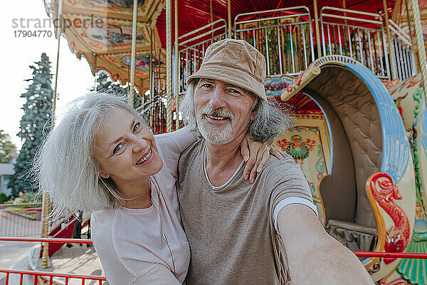 Glücklicher Mann macht Selfie mit Frau vor Karussell