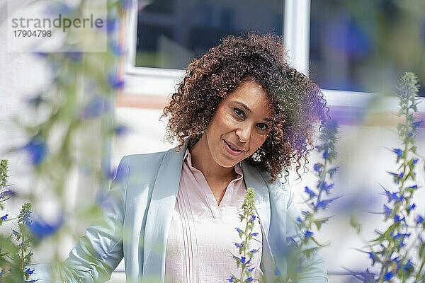 Reife Geschäftsfrau mit lockigem Haar neben Blumen