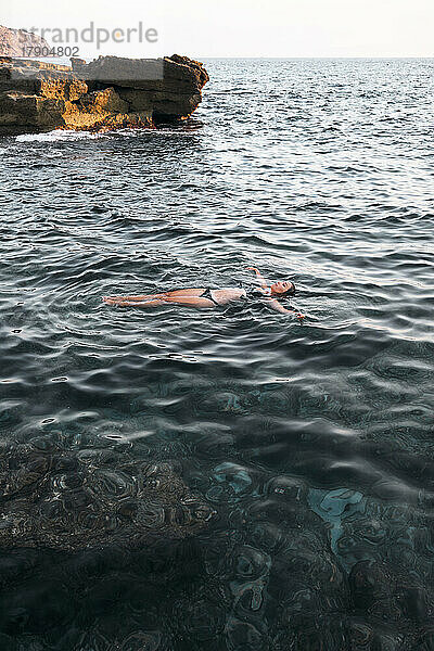 Frau schwimmt bei Sonnenuntergang im Meer