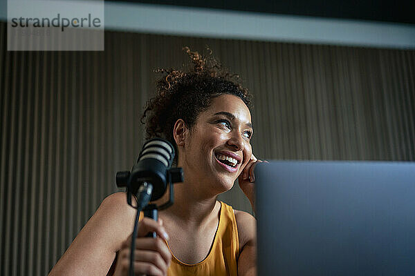 Happy radio presenter with microphone podcasting at workplace