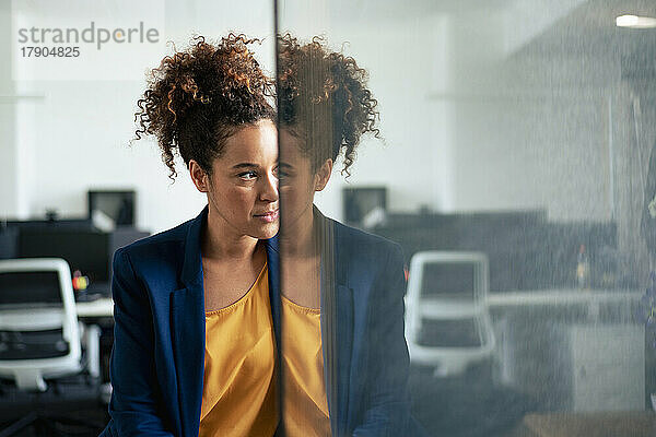 Nachdenkliche Geschäftsfrau mit Reflexion an der Glaswand im Büro