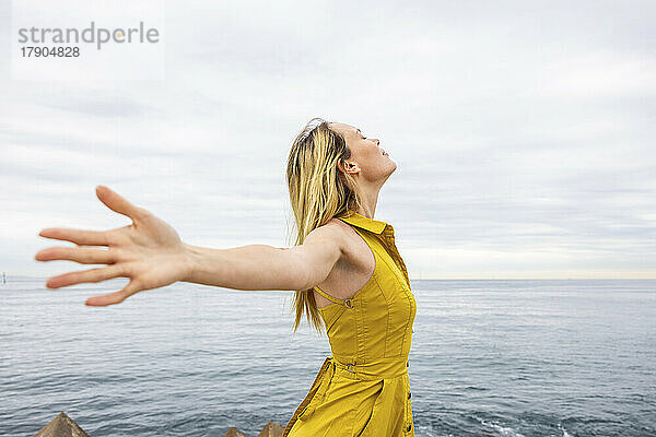Carefree woman with arms outstretched by sea