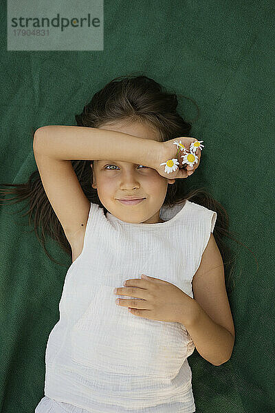 Lächelndes Mädchen mit Kamillenblüten auf einer Decke liegend