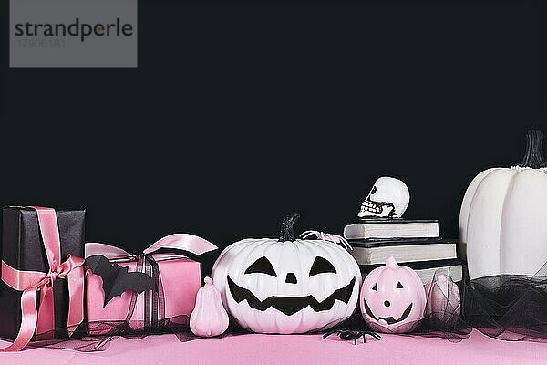 Rosa und weiße Halloween-Dekoration mit schwarzen und weißen Kürbissen  Zauberbücher und Spinnen auf schwarzem Hintergrund mit Kopierraum