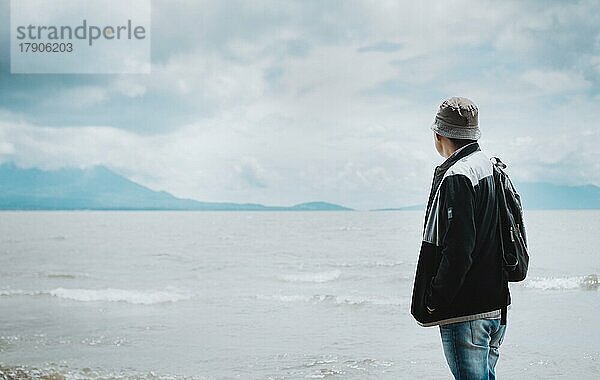 Rückansicht eines Touristen mit Blick auf einen See mit Vulkanen. Explorer Person mit Blick auf einen See an einem sonnigen Tag. Tourist Mann in Hut von hinten Blick auf einen See mit Vulkanen in Rivas  Nicaragua  Mittelamerika
