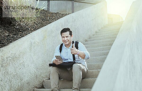 Junger Mann sitzt auf einer Treppe mit Handy und Daumen nach oben  Lächelnder Mann sitzt auf einer Treppe mit Handy und Daumen nach oben  Nahaufnahme von Person sitzt auf einer Treppe mit Handy und Daumen nach oben