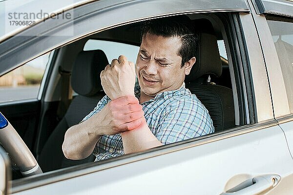 Fahrer leidet unter Schmerzen im Handgelenk. Wunde Fahrer Mann berührt sein Handgelenk. Fahrer mit Handschmerzen. Leidender Fahrer am Steuer  der sich den Arm reibt  weil er so viel fährt. Wunde Mann müde vom Fahren