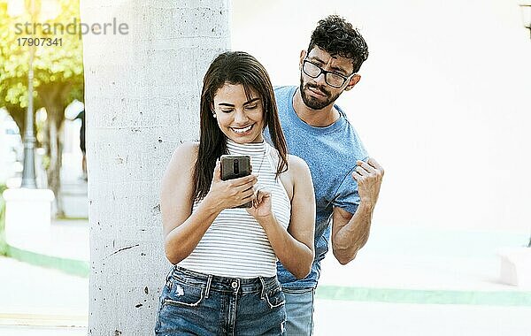Verdächtiger Mann spioniert seine Freundin mit seinem Handy aus  Eifersüchtiger Freund spioniert das Handy seiner Freundin im Park aus. Eifersüchtiger Mann spioniert seiner Freundin auf dem Handy SMS schreiben