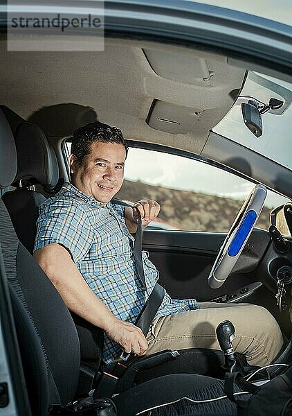 Glücklicher Fahrer beim Anlegen des Sicherheitsgurtes  Lächelnder männlicher Fahrer beim Anlegen des Sicherheitsgurtes. Konzept eines Fahrers in seinem Auto  der sich anschnallt. Lächelnde Person beim Anlegen des Sicherheitsgurtes