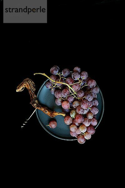 Rote Weintrauben (Vitis vinifera) mit Korkenzieher vor dunklem Hintergrund