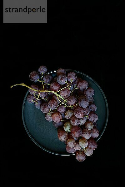 Rote Weintrauben (Vitis vinifera) auf Teller vor dunklem Hintergrund