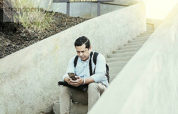 A guy sitting on stairs using his cell phone outdoors with copy space  Young man sitting on stairs using smart phone  Close up of young man sitting on stairs texting on cell phone outdoors