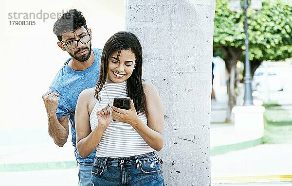 Eifersüchtiger Mann spioniert seine Freundin aus  die mit dem Handy SMS schreibt. Verdächtiger Mann spioniert seine Freundin mit seinem Handy aus  Eifersüchtiger Freund spioniert das Handy seiner Freundin im Park aus