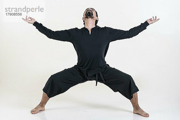 Ein Mann in schwarz gekleidet tun Yoga über weißem Hintergrund. Utkata konasana Yoga-Pose. Studioaufnahme
