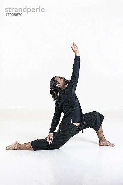 Ein Mann in schwarz gekleidet macht Yoga über weißem Hintergrund. anjaneyasana Yoga-Pose. Studioaufnahme