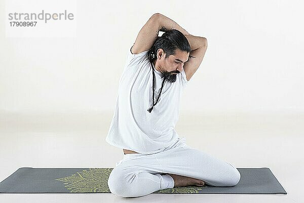 Ein weiß gekleideter Mann macht Yoga auf einer Matte vor weißem Hintergrund. bharadvajasana Yoga-Pose. Studioaufnahme