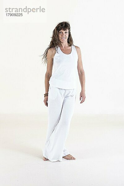 Porträt einer Frau in weißer Yoga-Kleidung vor weißem Hintergrund  die in die Kamera schaut. Studioaufnahme