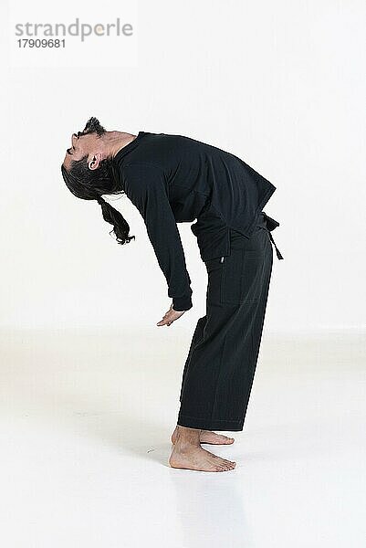 Ein Mann in schwarz gekleidet macht Yoga über weißem Hintergrund. Suryanamaskar Yoga-Pose. Studioaufnahme