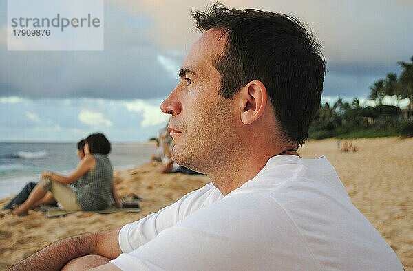 Seitenansicht eines jungen  gut aussehenden Mannes  der den Sonnenuntergang in Sunset Beach  Oahu  Hawaii  USA beobachtet