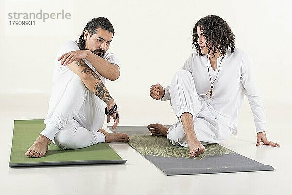 Ein Yogalehrer unterrichtet einen jungen Mann in Yoga. Beide sind mit weißer Yogakleidung bekleidet. Vorderansicht