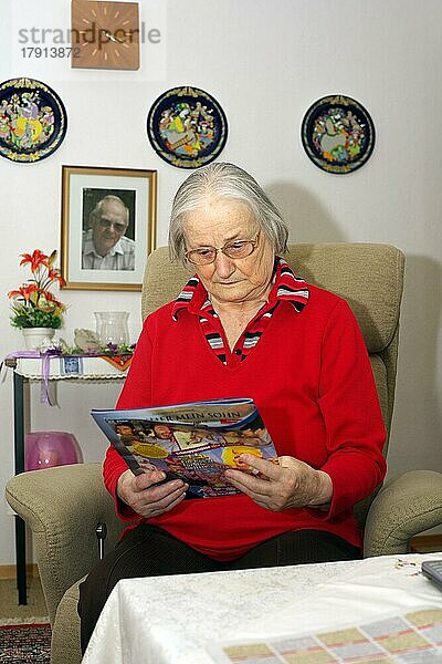 Alte Frau  Seniorin  84 Jahre  liest im Wohnzimmer alleine Illustrierte  München  Bayern  Deutschland  Europa