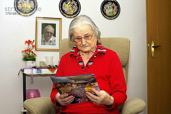 Alte Frau  Seniorin  84 Jahre  liest im Wohnzimmer alleine Illustrierte  München  Bayern  Deutschland  Europa
