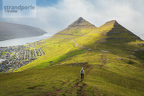 Wanderer mit gelber Jacke wandert den Berg Klakker hinunter  Klaksvik  Insel Borooy  Färöer Inseln  Dänemark  Europa